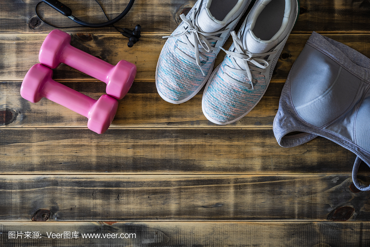 女性健身和积极健康的生活方式锻炼背景概念。训练鞋,粉色哑铃,运动胸罩,和耳机的木制背景。平放顶视图与复制空间。